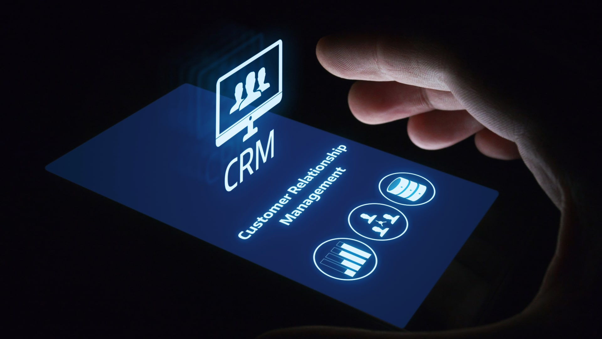 A hand hovering over a smartphone screen displaying the acronym "CRM" and the words "Customer Relationship Management" with icons representing customer data, analytics, and team collaboration.