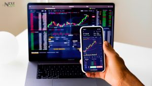 "Smartphone displaying live stock charts in the foreground with a laptop showing market data in the background, and Showing a stock trading app development in 2025."