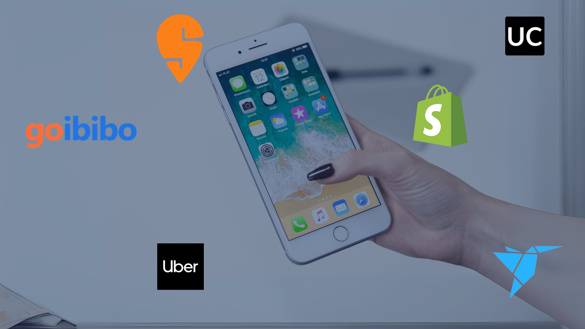 A hand holding a smartphone with app icons on the screen, surrounded by logos of popular on-demand service apps like Uber, Shopify, Goibibo, and Freelancer, representing on-demand app development trends.